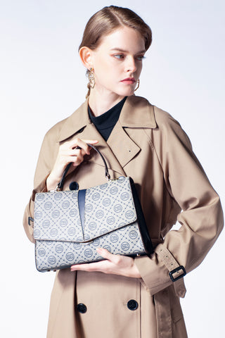 A luxurious women's handbag with light gray and blue patterns is carried by a woman in a beige coat.