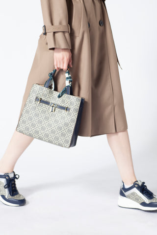 A model showing a Saga handbag in gray color with a circular pattern and a blue handle, matching clothes