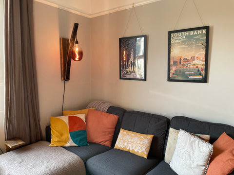 A whiskey stave wall light with a maroon LED light bulb casting a cosy glow over ta corner sofa