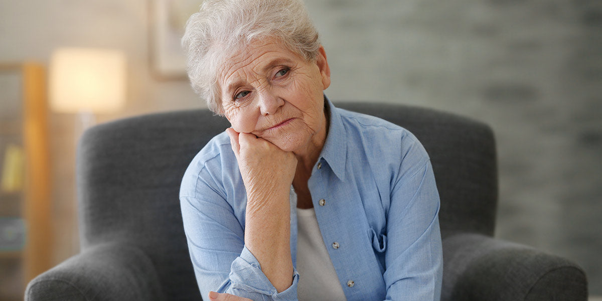 Depressed elderly woman sitting in arm-char at home