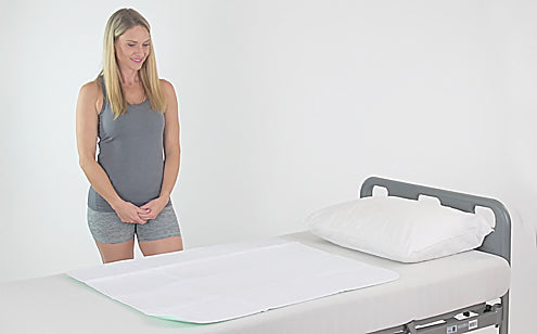 Mujer de mediana edad de pie junto a una cama con almohadilla de incontinencia reutilizable