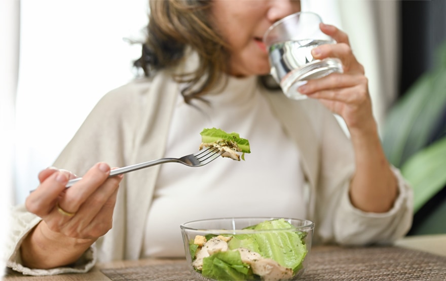Healthy and happy Asian-aged eating salad bowl and drinking water 