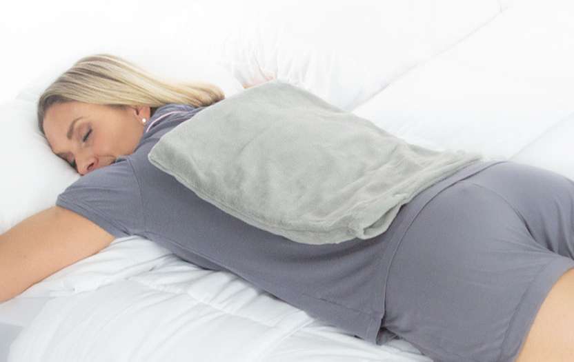 Woman sleeping on a bed with heating pad on her back
