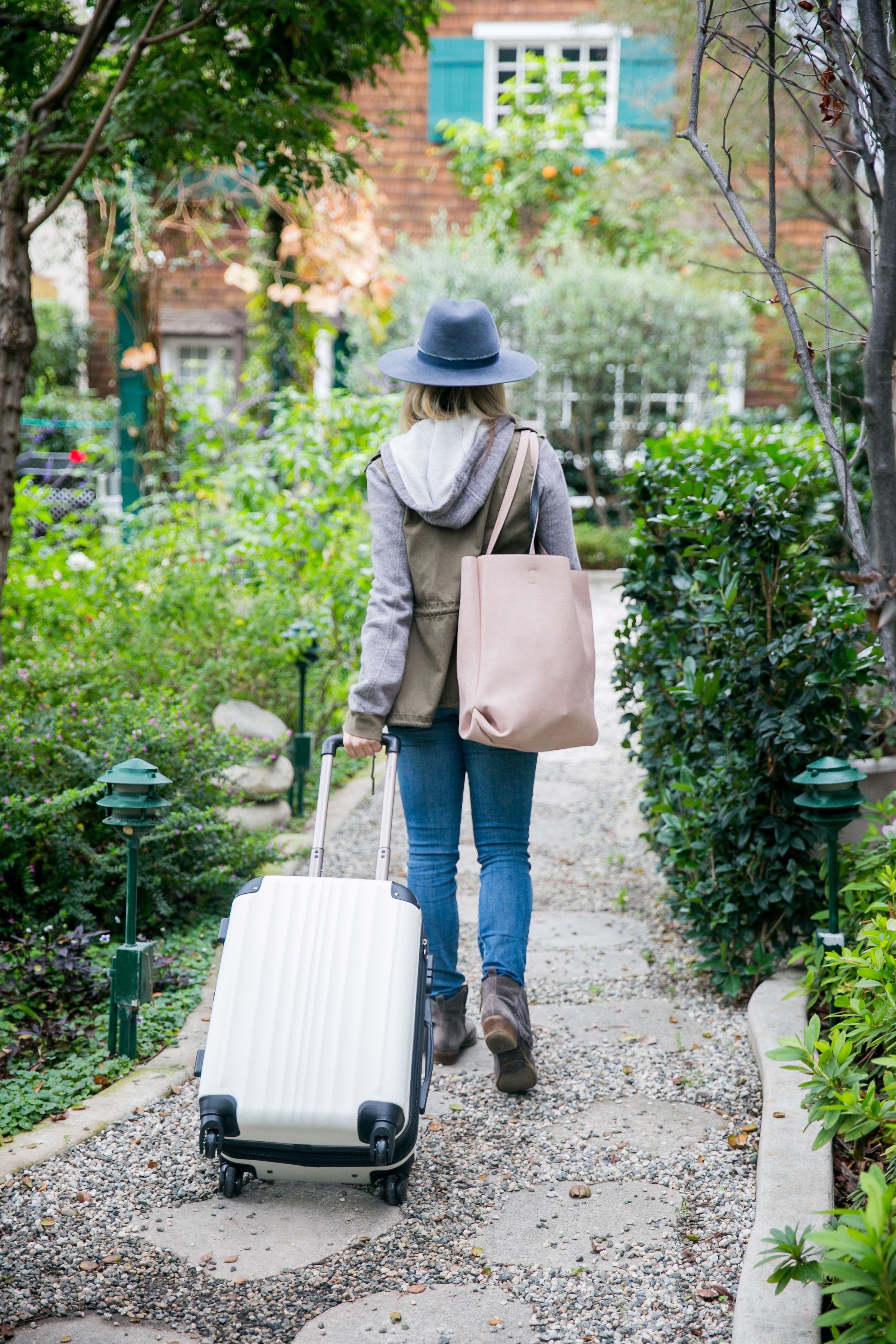 Lady wearing a jacket and a hat carrying a tote bag and carry-on suitcase