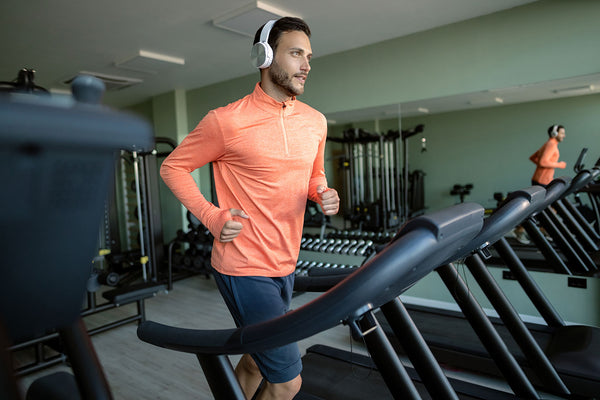Determined male athlete with headphones running on treadmill in a gym.