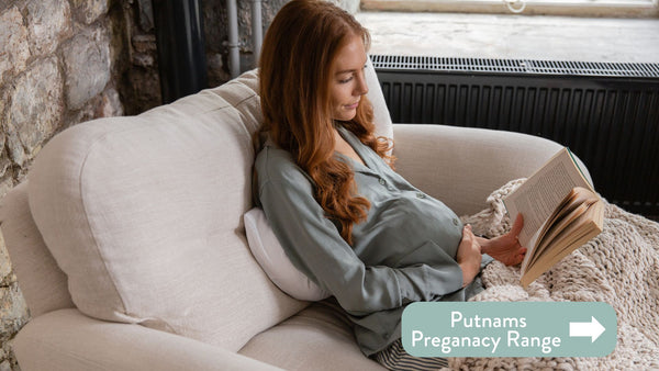 Person sitting on a sofa reading a book supported by a Putnams pregnancy cushion