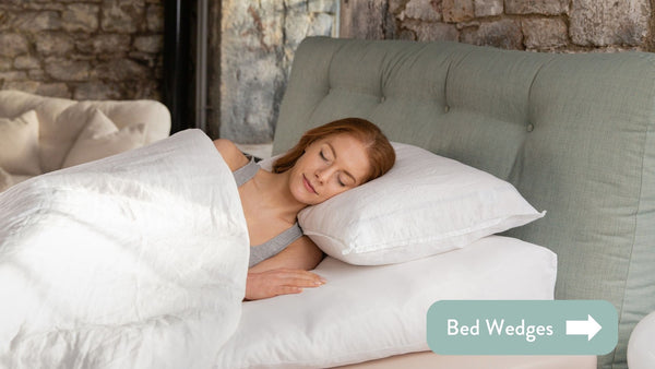 person in bed with white linen using a Putnams bed wedge with a teal cushioned headboard