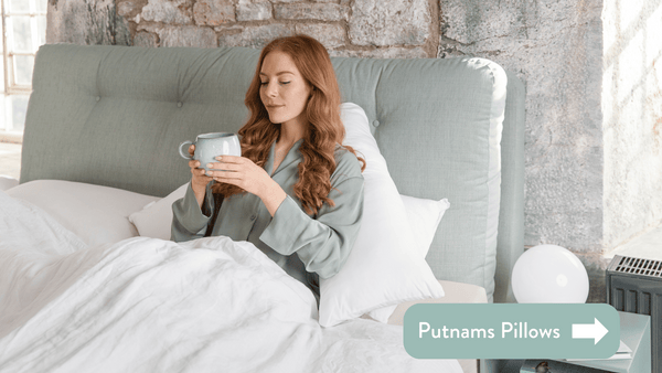 Person drinking tea to relive acid reflux and heartburn in bed with white bedsheets and teal headboard against stone walls