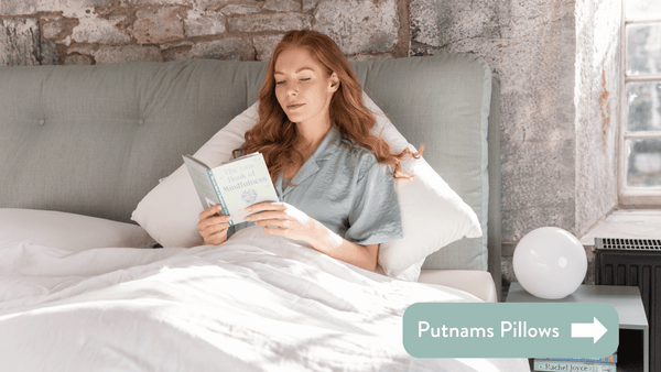 Person lying in bed reading a book wearing teal coloured pyjamas on white linen