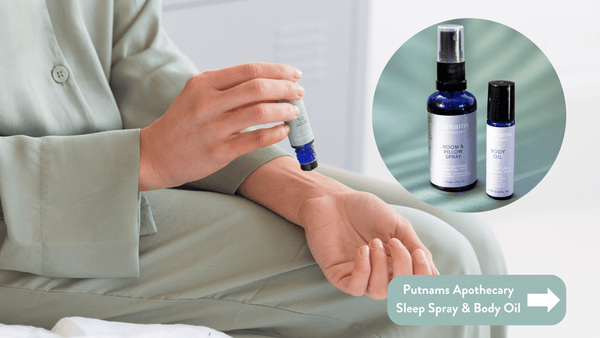 Person putting on some of the Putnams Apothecary Sleep Spray & Body Oil in a blue bottle wearing teal satin pyjamas