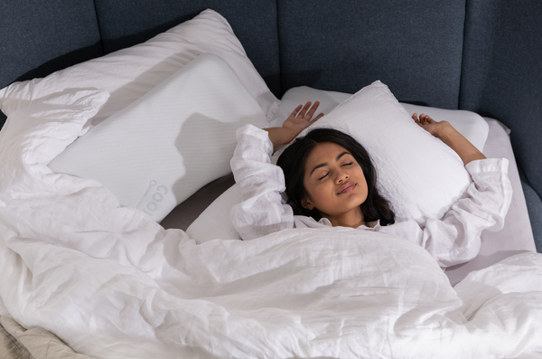 Person lying in a bed with white linen and a navy blue head board