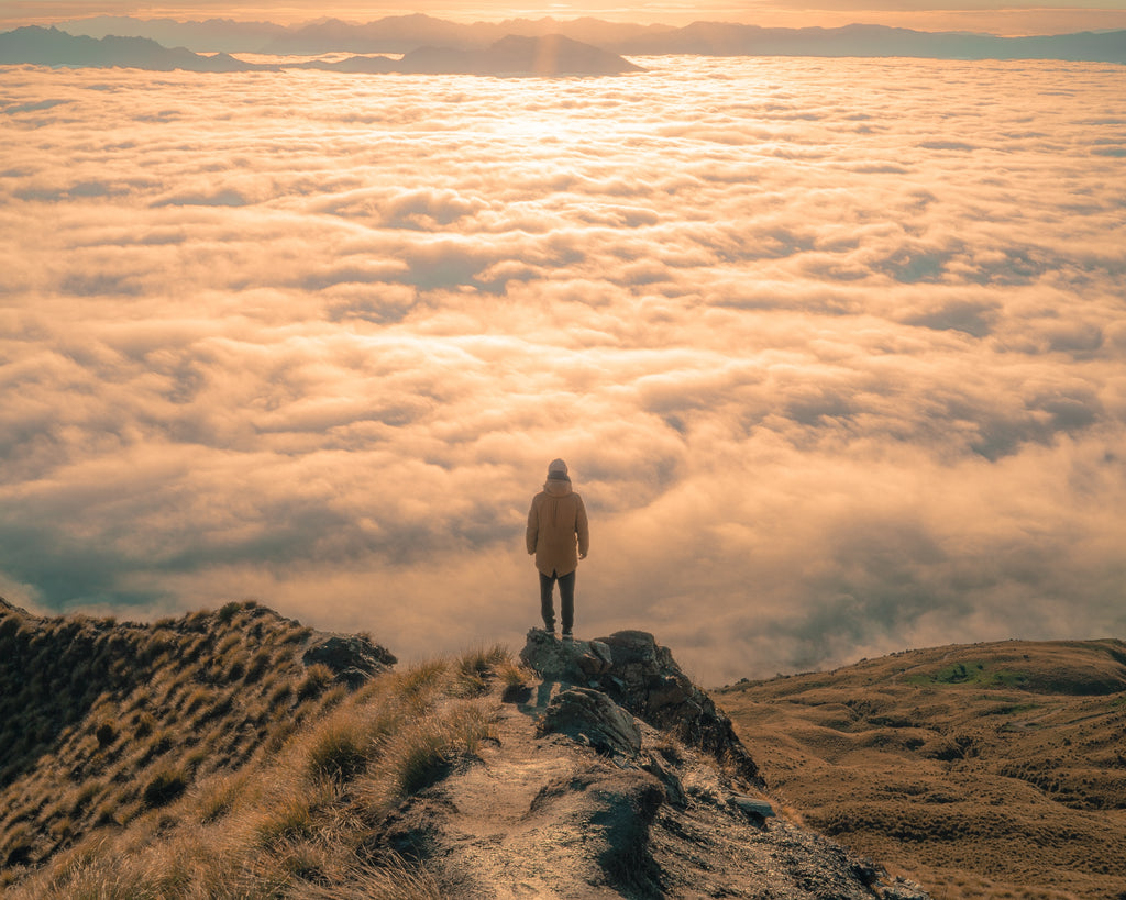 a person standing on a mountain peak above cloud level looking out onto the wonderful vista proving that anything is possible when managing Seasonal Affective Disorder SAD