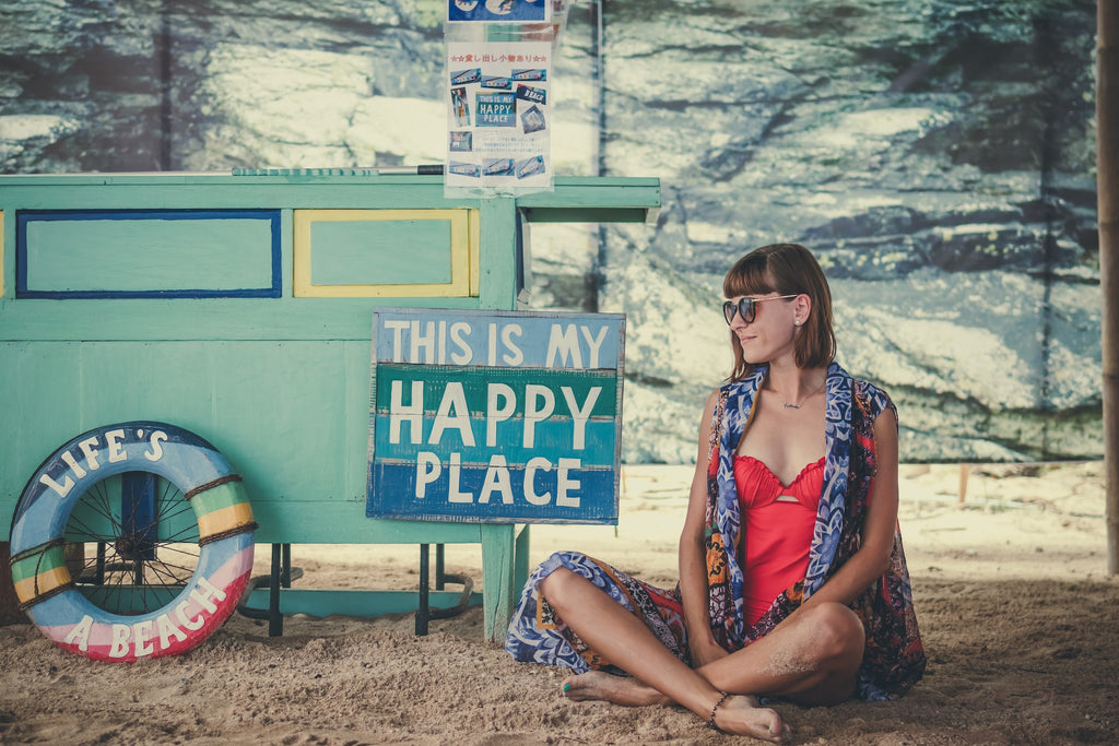 Person sitting on beach cross legged with My Happy Place sign next to them