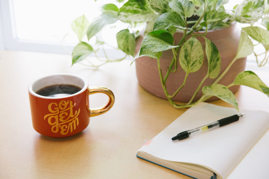 a coffee cup and pen and diary on a wooden desk showing the importance of setting achievable goals when coping with seasonal affective disorder