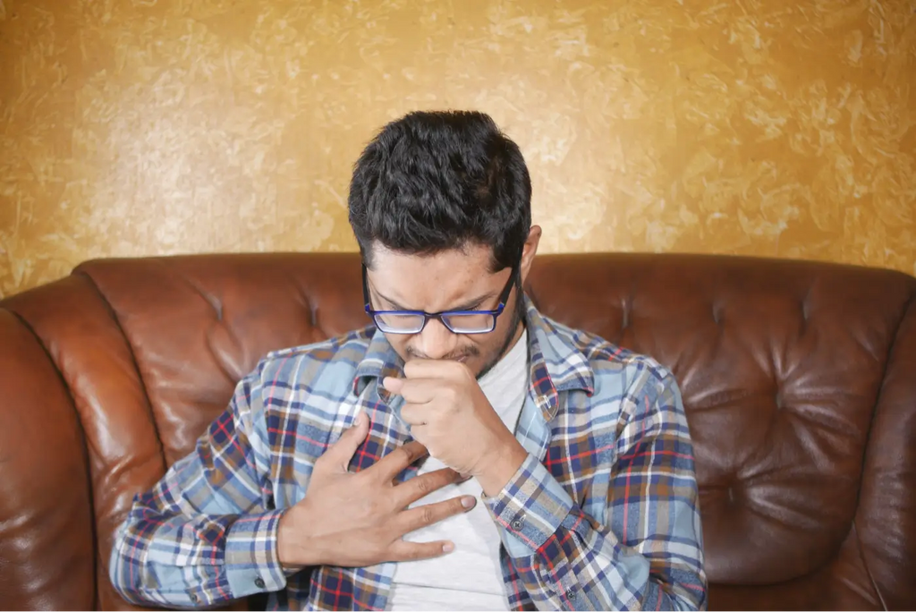 jeune homme avec lunettes assis sur un canapé marron qui tousse