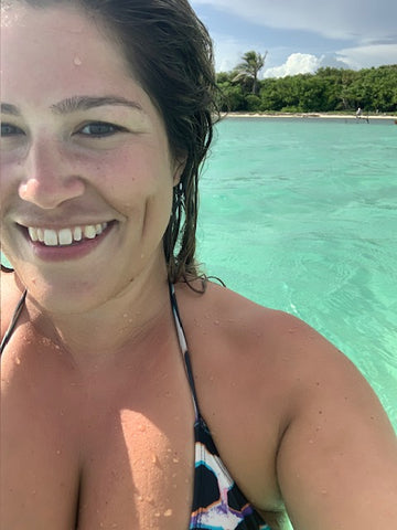 Selfie of a woman in the crystal clear blue Sian Ka'an waters with the shore in the background.