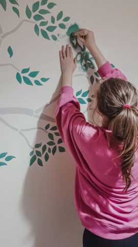 Decorating child's bedroom wall by adding leaves to the tree stencil design 