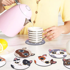 Pink kettle pouring water into striped cup on table with cat shaped diamond painting coasters.