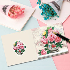 Diamond painting of pink flower bouquet with blue flowers in background and pen on sketchbook