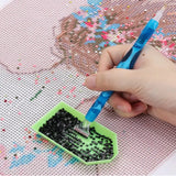 Hand met een diamond painting pen plaatst zwarte steentjes vanuit een groene sorteerbakje op een canvas met patroon