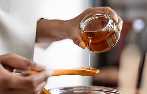 A person pouring honey into a pot with a wooden spoon