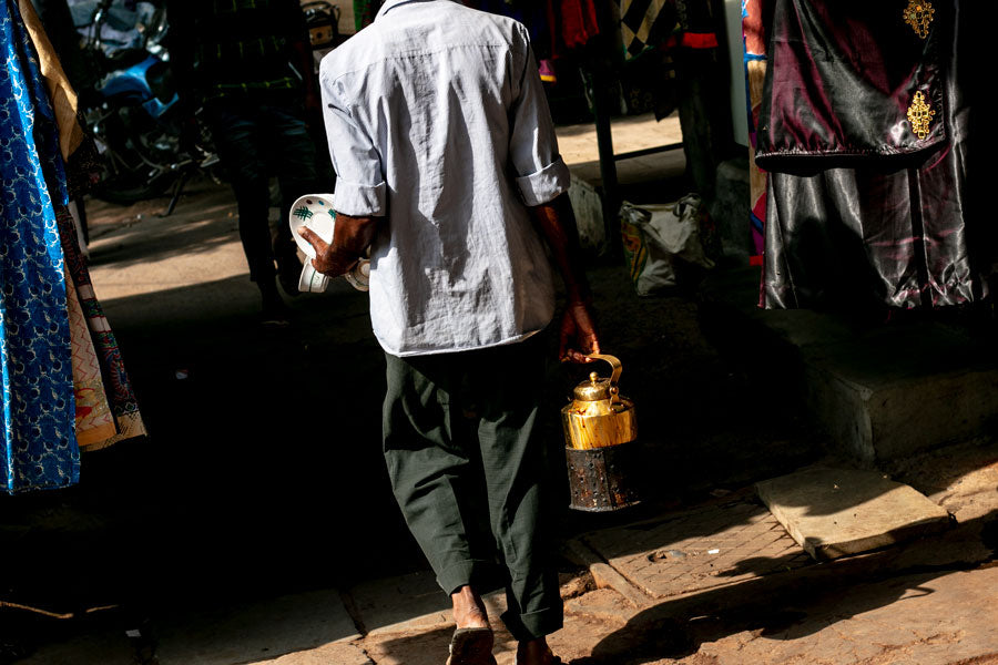 Vendeur de chaï de dos qui marche dans la rue, une grosse théière à la main