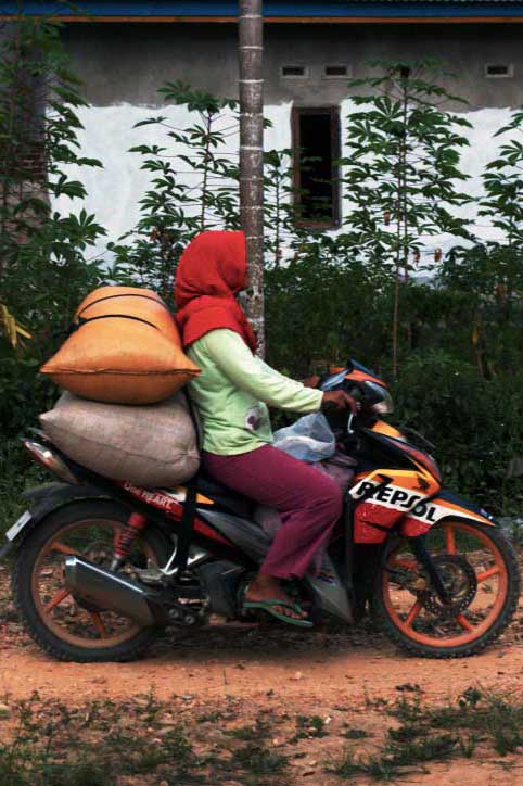 Productrice sur une moto, chargée à l'arrière de sac de poivre