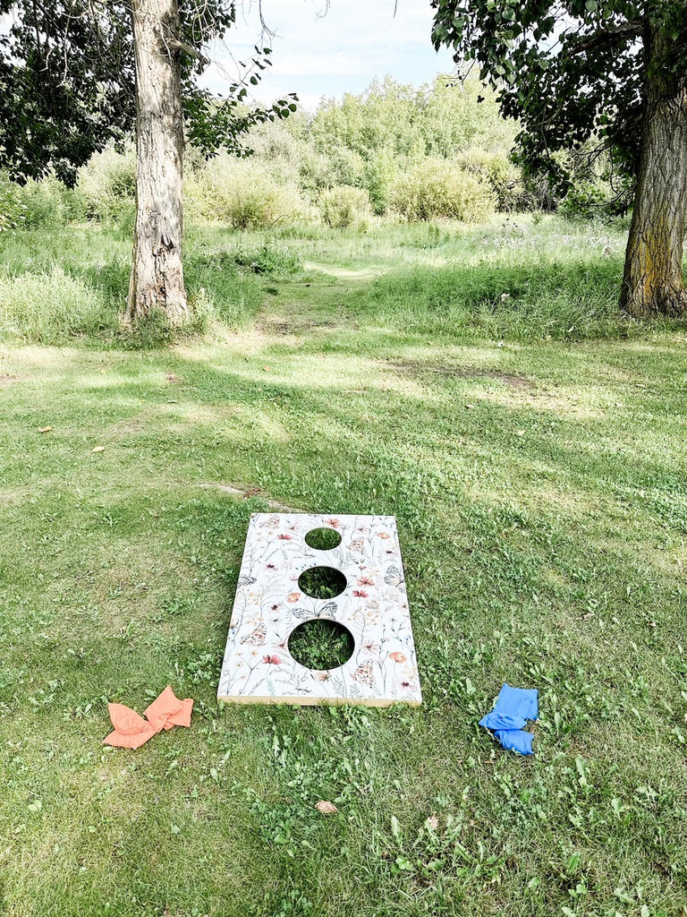 Playing corn hole on a custom game board decorated with floral butterfly peel and stick wallpaper