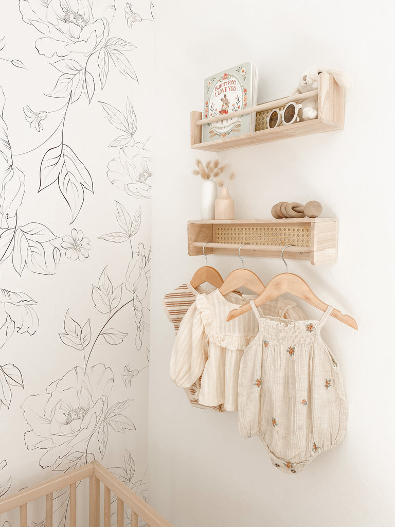 Baby girl nursery with floral peel and stick wallpaper, wooden shelves and crib