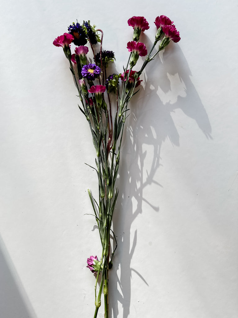 Variety of fresh-cut flowers with vibrant carnations and dark blue accents laid out for a DIY Costco flower bouquet project.