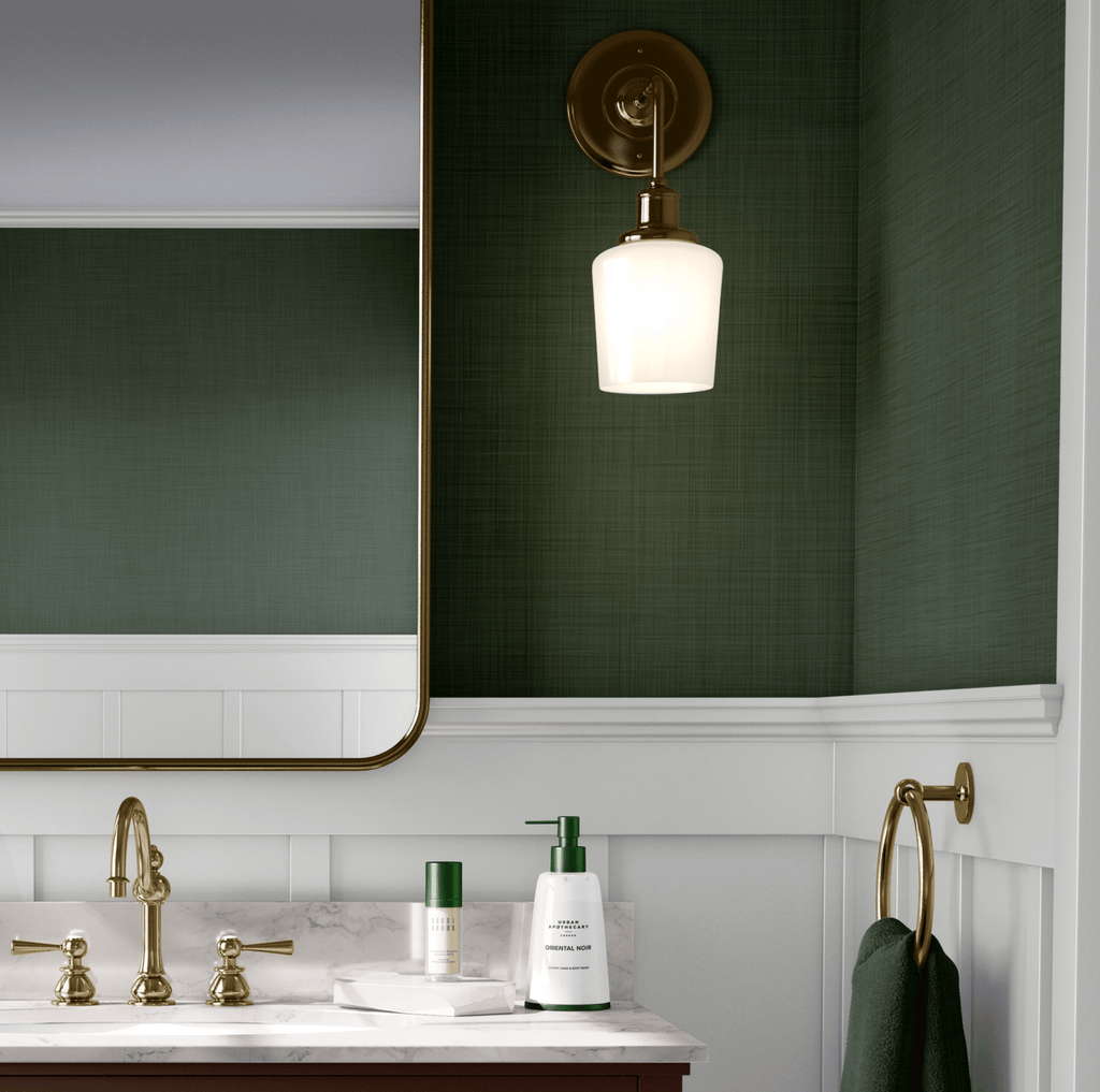 Elegant bathroom with forest green grasscloth peel and stick wallpaper, white wainscoting, and brass accents. A brass sconce illuminates the textured wallpaper, enhancing the luxurious feel of the space