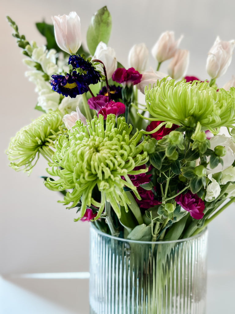 Assorted fresh spring bouquet in a ribbed glass vase showcasing green spider mums, white tulips, and richly colored accent flowers for a DIY Costco floral arrangement.