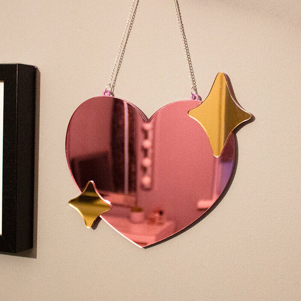 Sprinkle Club - A small pink love heart shaped mirror with gold sparkles hanging on a wall