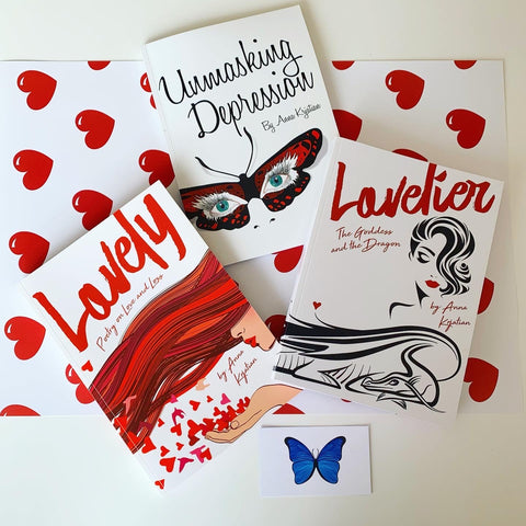 Three books (Unmasking Depression, Lovely - Poetry on Love and Loss and Lovelier - The Goddess and The Dragon) and a blue butterfly logo sit on top of a white table and Lovely Wrapping Paper with red hearts dispersed throughout it.