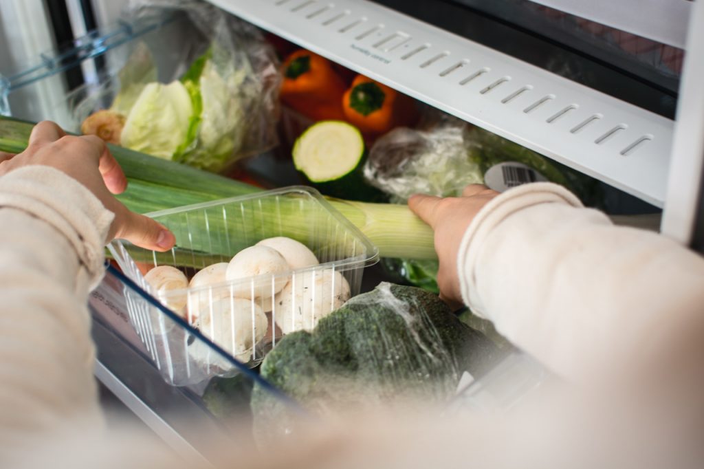 A hand storing vegetables in a refrigerator chiller