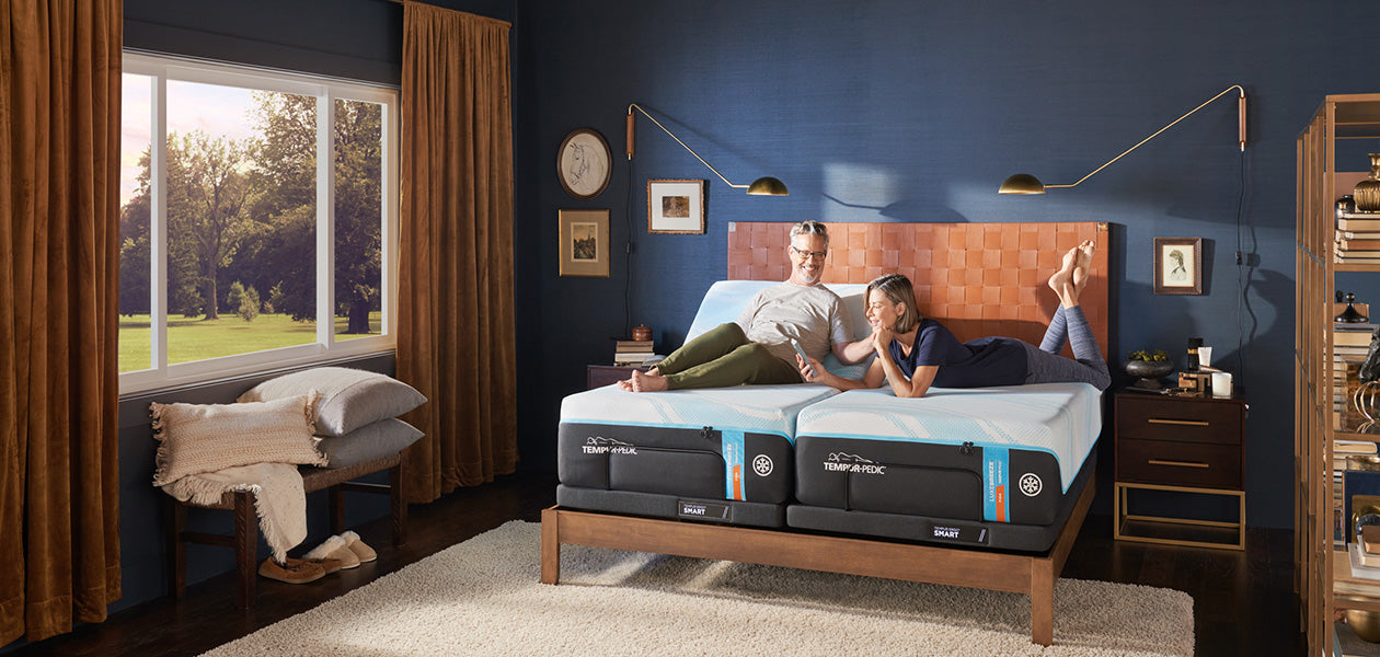 A couple laying on a Luxe Breeze Firm split king mattress in a luxuriously decorated dark blue bedroom with orange accents