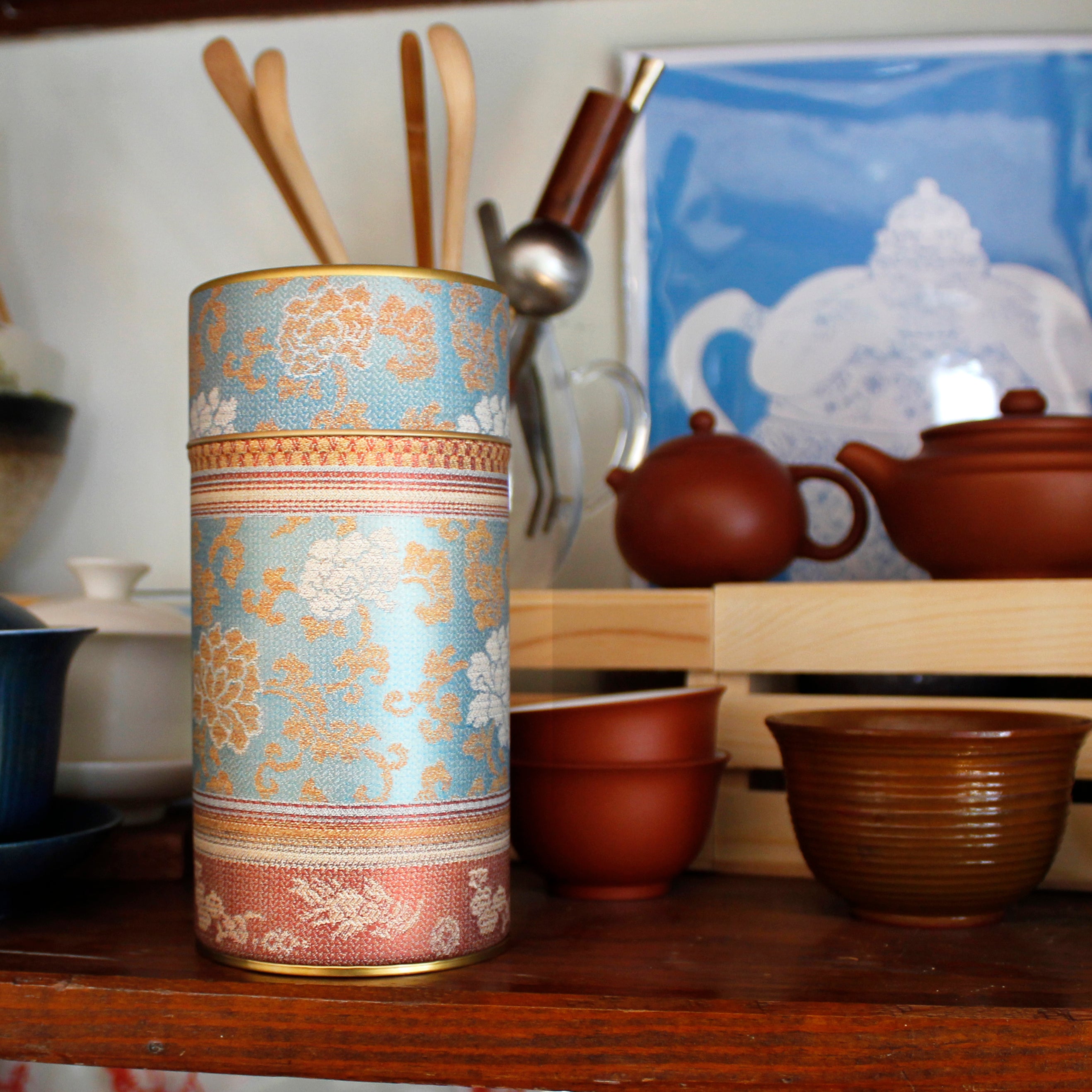 A beautiful peony-print, blue tea storage tin sits amongst teapots and tea accessories.