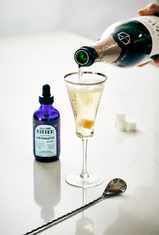 champagne flute being poured with non-alcoholic bitters next to it