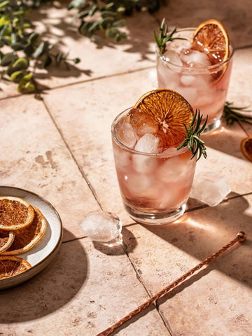 Dried orange iced summer cocktails with rosemary and beautiful shadows on tile background