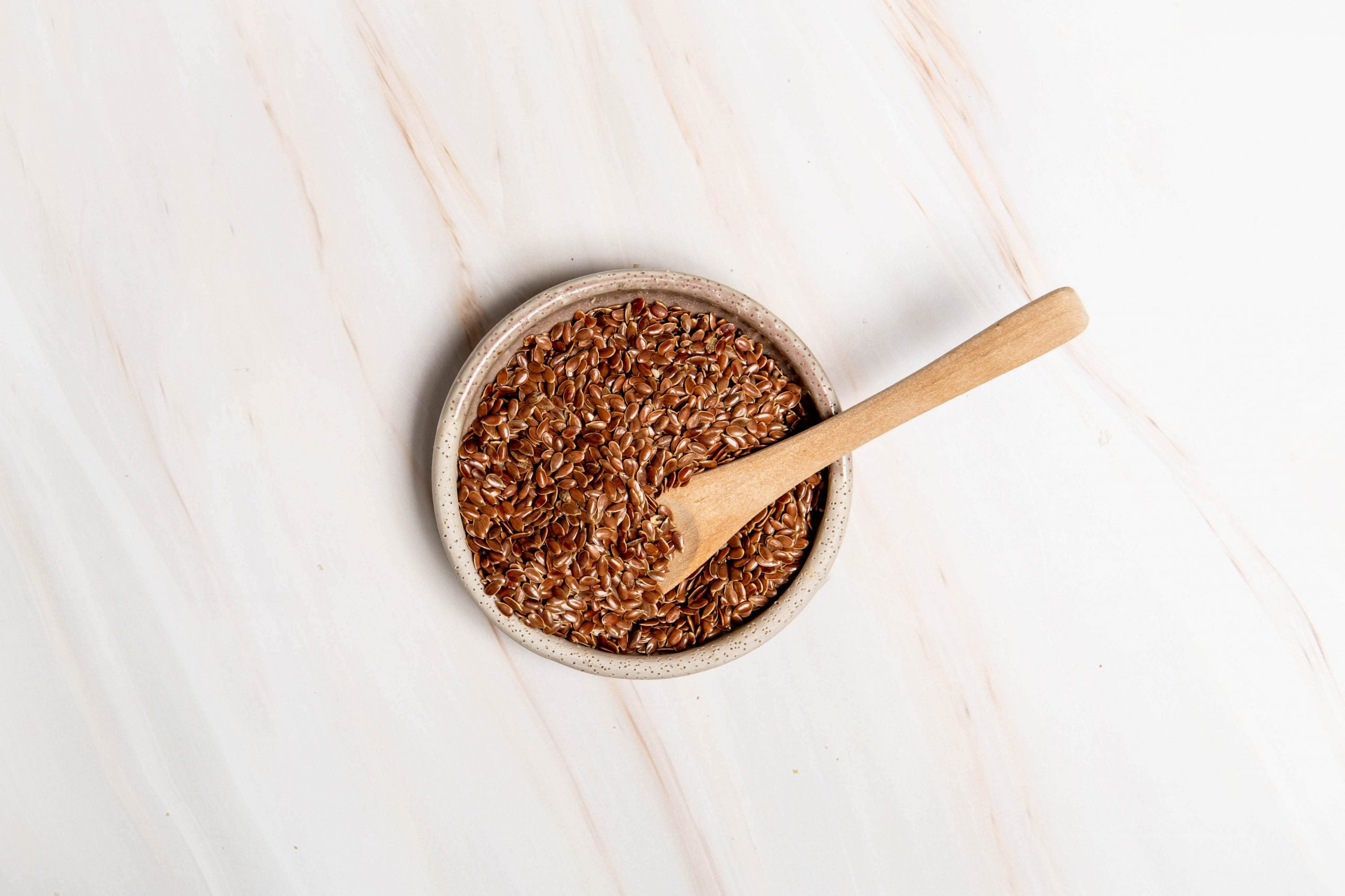 A bowl of flax seeds sitting on a kitchen bench with a wooden spoon in the bowl. What are the benefits of seed cycling?