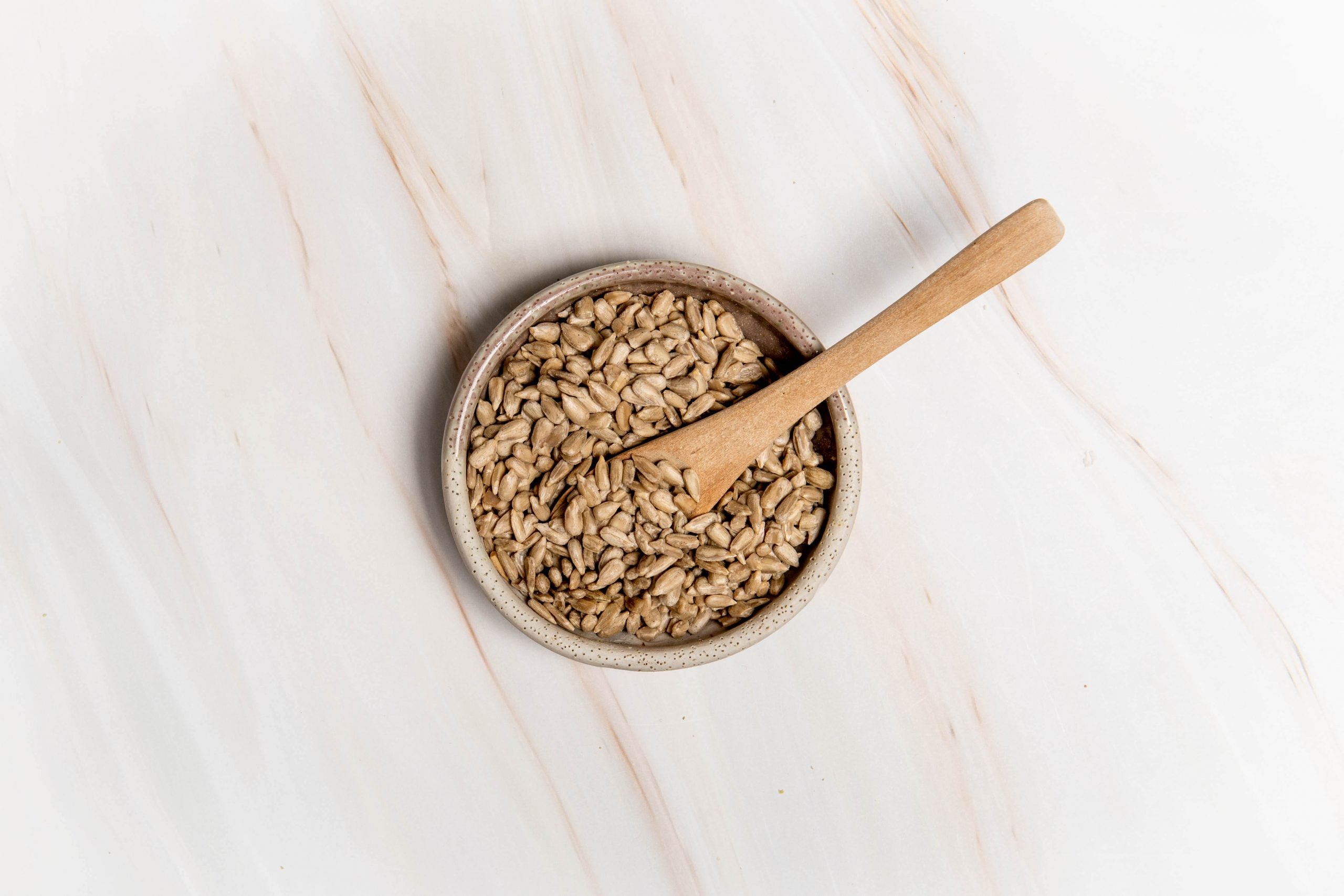 A bowl of sunflower seeds sitting on a kitchen bench with a wooden spoon in the bowl. How to seed cycle.