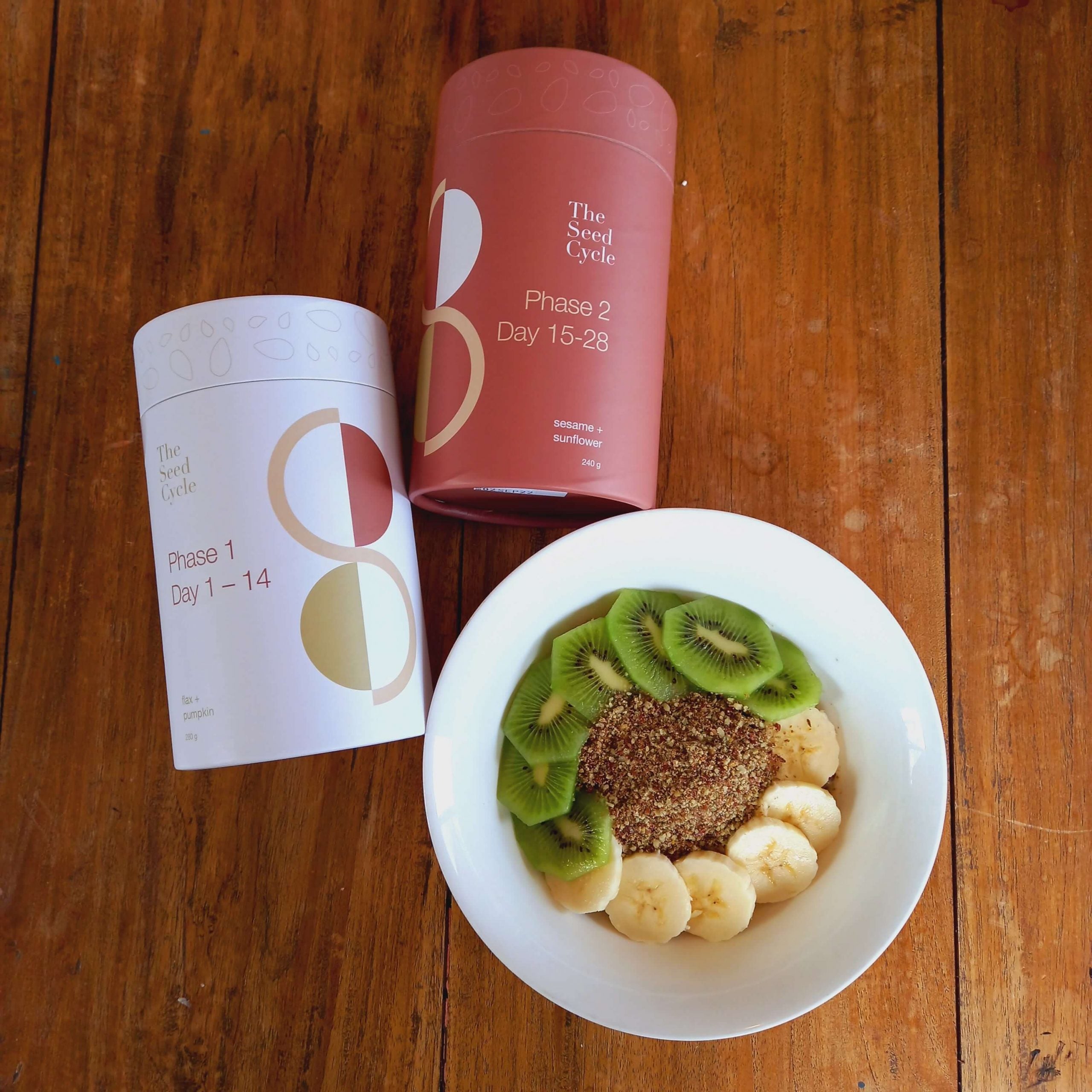 flatlay phase 1 and phase 2 containers of The Seed Cycle and bowl with overnight oats, kiwi fruit and banana