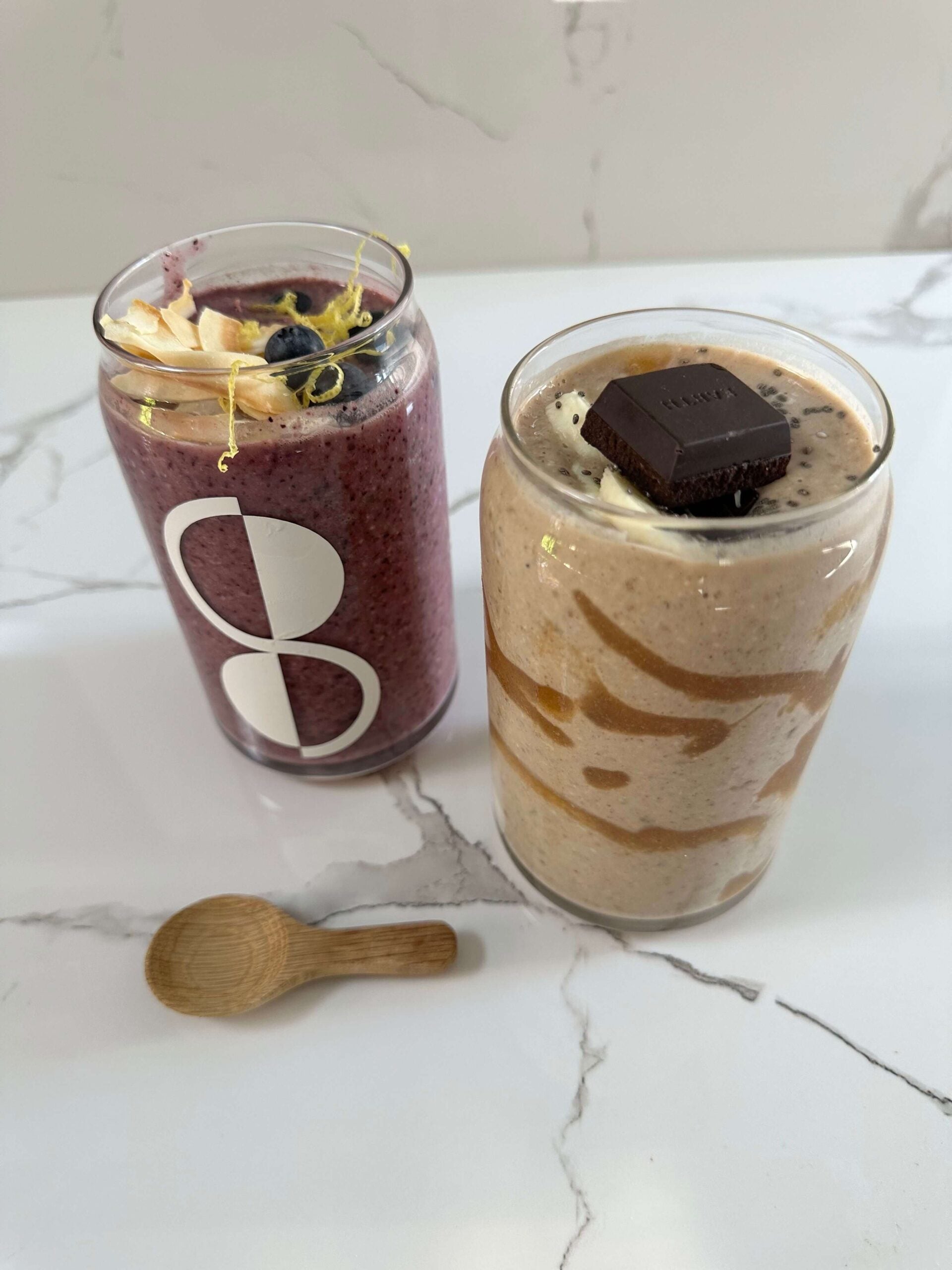 two glasses one with seed cycling berry smoothie and other with banana and date smoothie on marble back drop