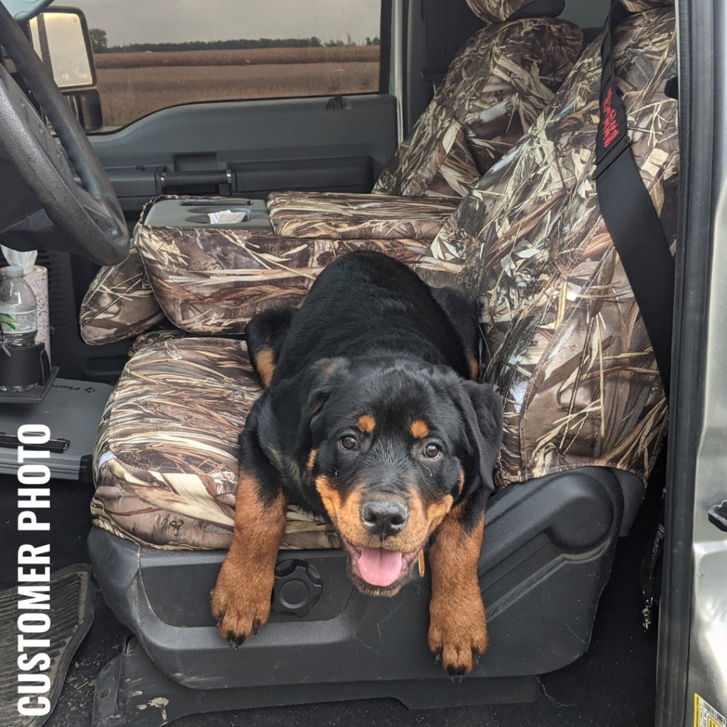 Rottweiler looking dog in the driver's seat of a truck with camo TigerTough seat covers.