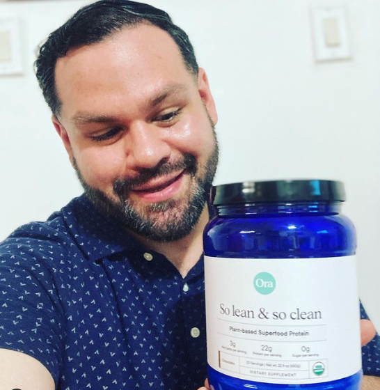 A man smiling and holding a jar of plant-based superfood protein.