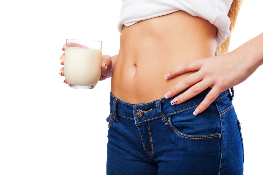 young woman's body with opened stomach, white top and blue jeans holding a glass with white liquid