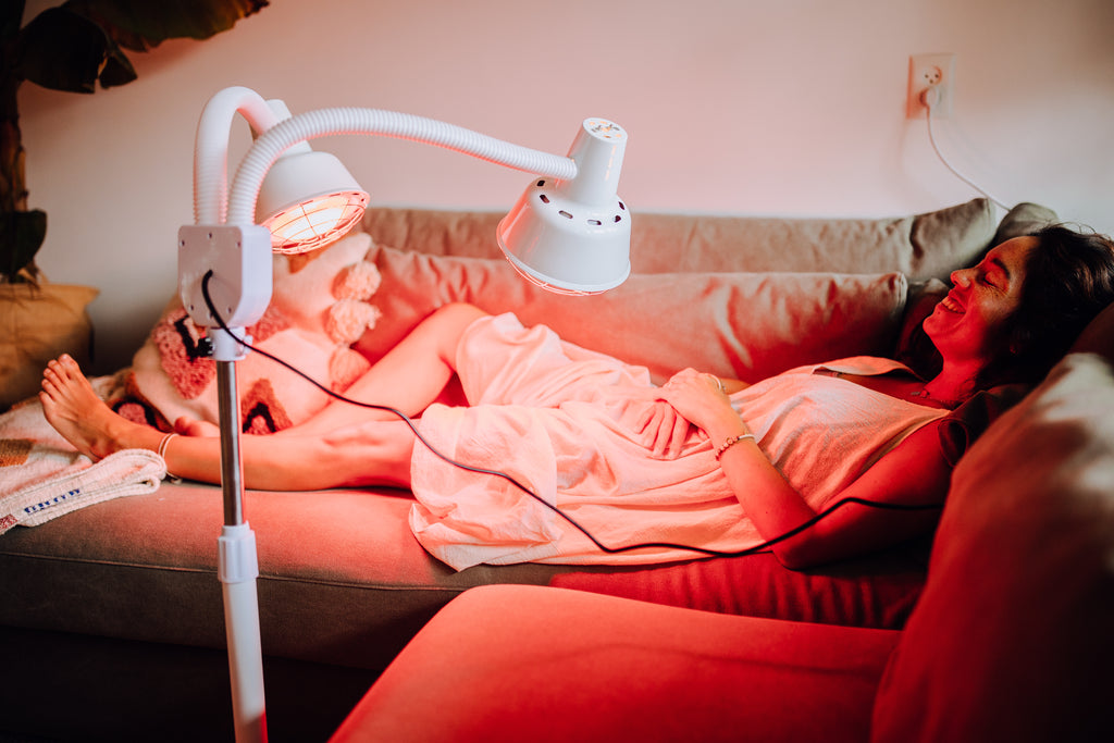 Woman lying down using infrared lamp on the couch with a blanket