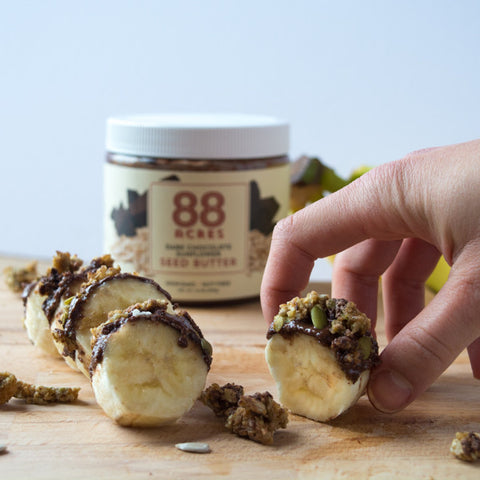 Sliced banana with dark chocolate sunflower seed butter spread, seednola, and pumpkin seeds. Easy, vegan recipe for breakfast or picnics.