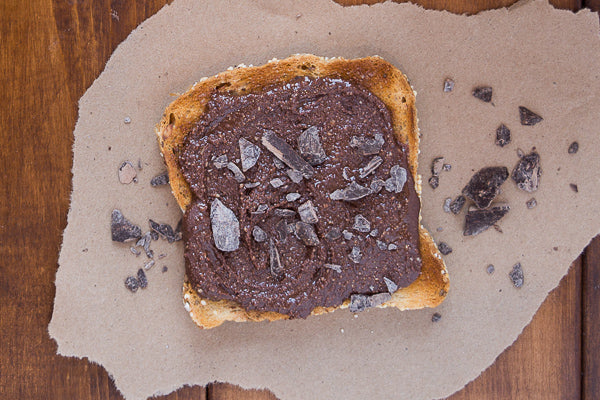 Dark chocolate sunflower seed butter spread  on slice of toasted bread, with pieces of dark  chocolate. Double the dose of micronutrients.