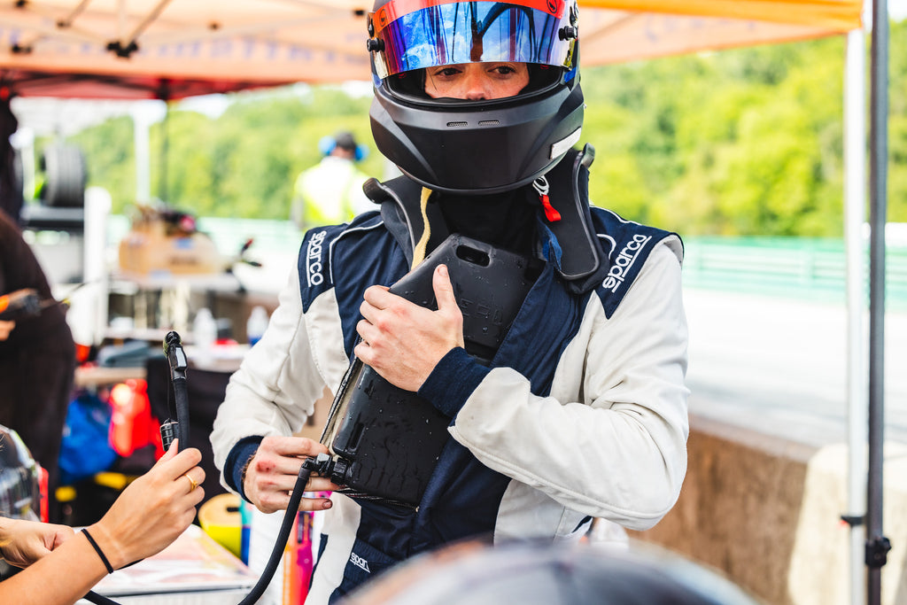 Man in Nomex Racing suit and racing helmet puts cooling and hydration bladder inside suit.